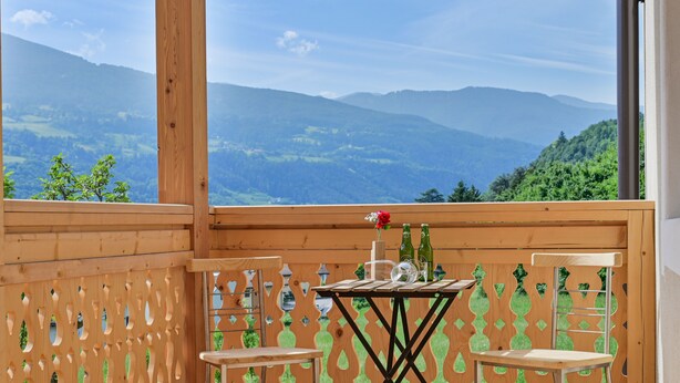 Un balcón de madera con una mesa y dos sillas, con vistas a un paisaje montañoso.