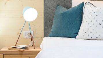 Un lit bien fait, avec un oreiller blanc à motifs, un oreiller turquoise et une lampe de chevet ronde posée sur une table de chevet en bois.