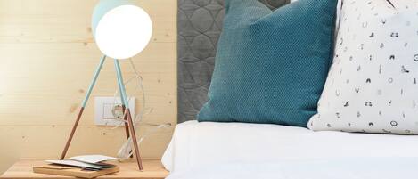 A neatly made bed with a white and patterned pillow, a teal pillow, and a round bedside lamp on a wooden nightstand.
