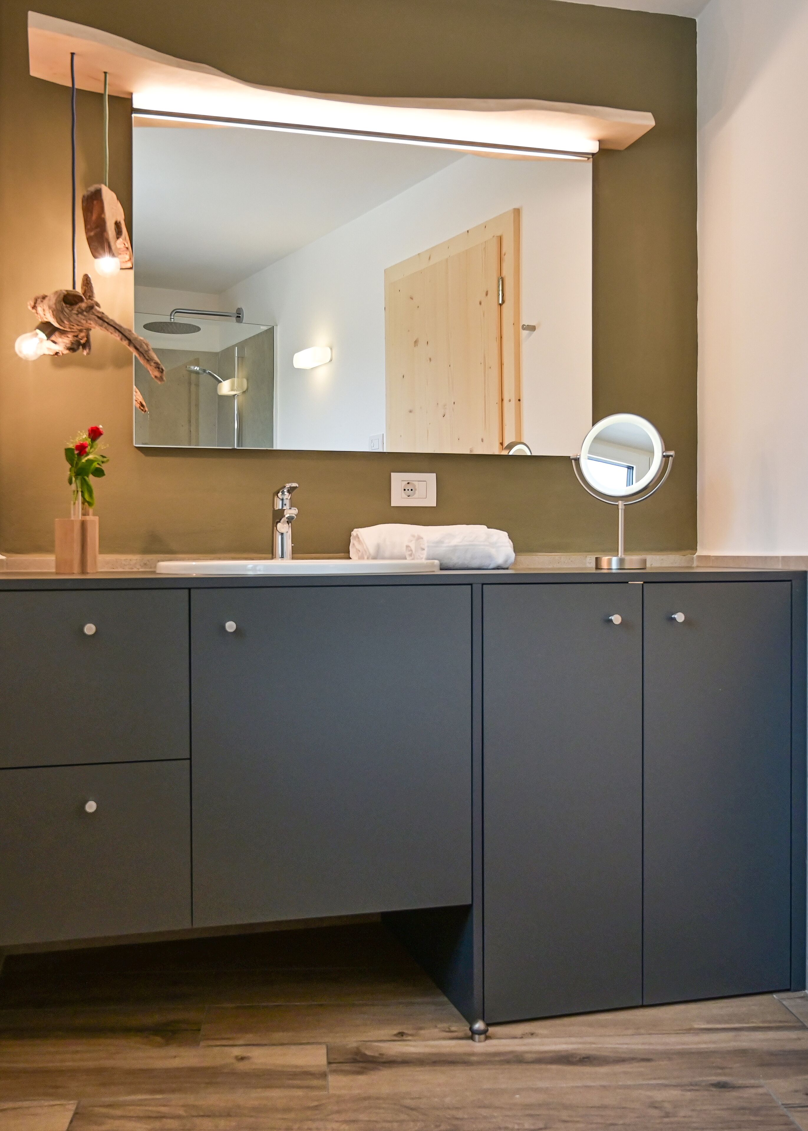 Un baño moderno con un mueble de tocador gris oscuro, un espejo grande y un espejo redondo pequeño.