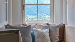 Una habitación con un ventanal que da a un pueblo y colinas. Hay varios almohadones en un banco.