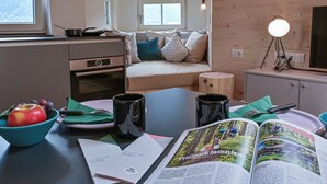 Una habitación acogedora con una cama, una mesa de comedor con un libro, un frutero y dos tazas.