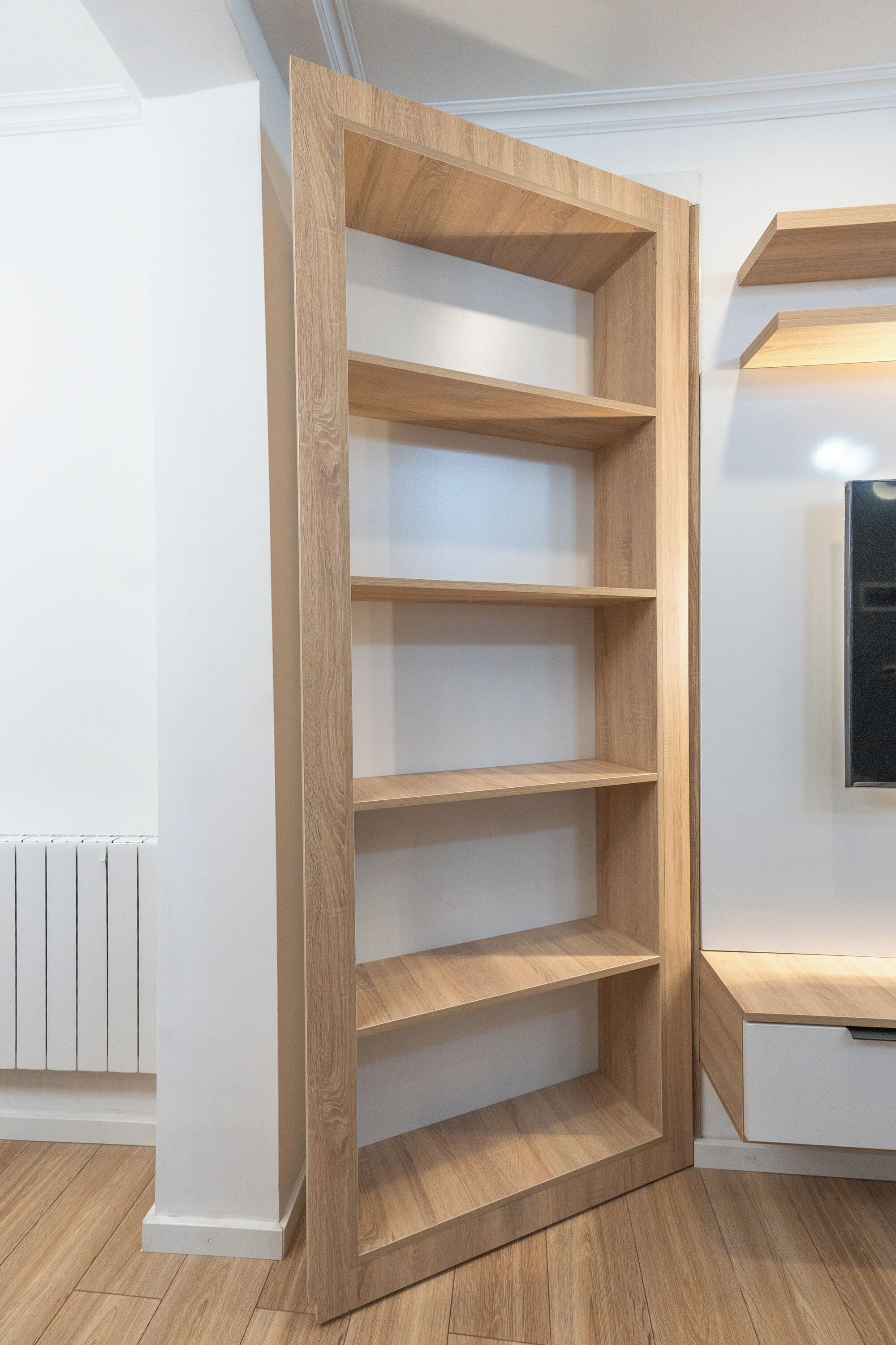 A wooden shelving unit with multiple open shelves, a white radiator, and a white wall.