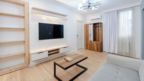 Moderni olohuone, jossa on litteänäyttöinen televisio, puuhyllyt, sohva ja sohvapöytä.