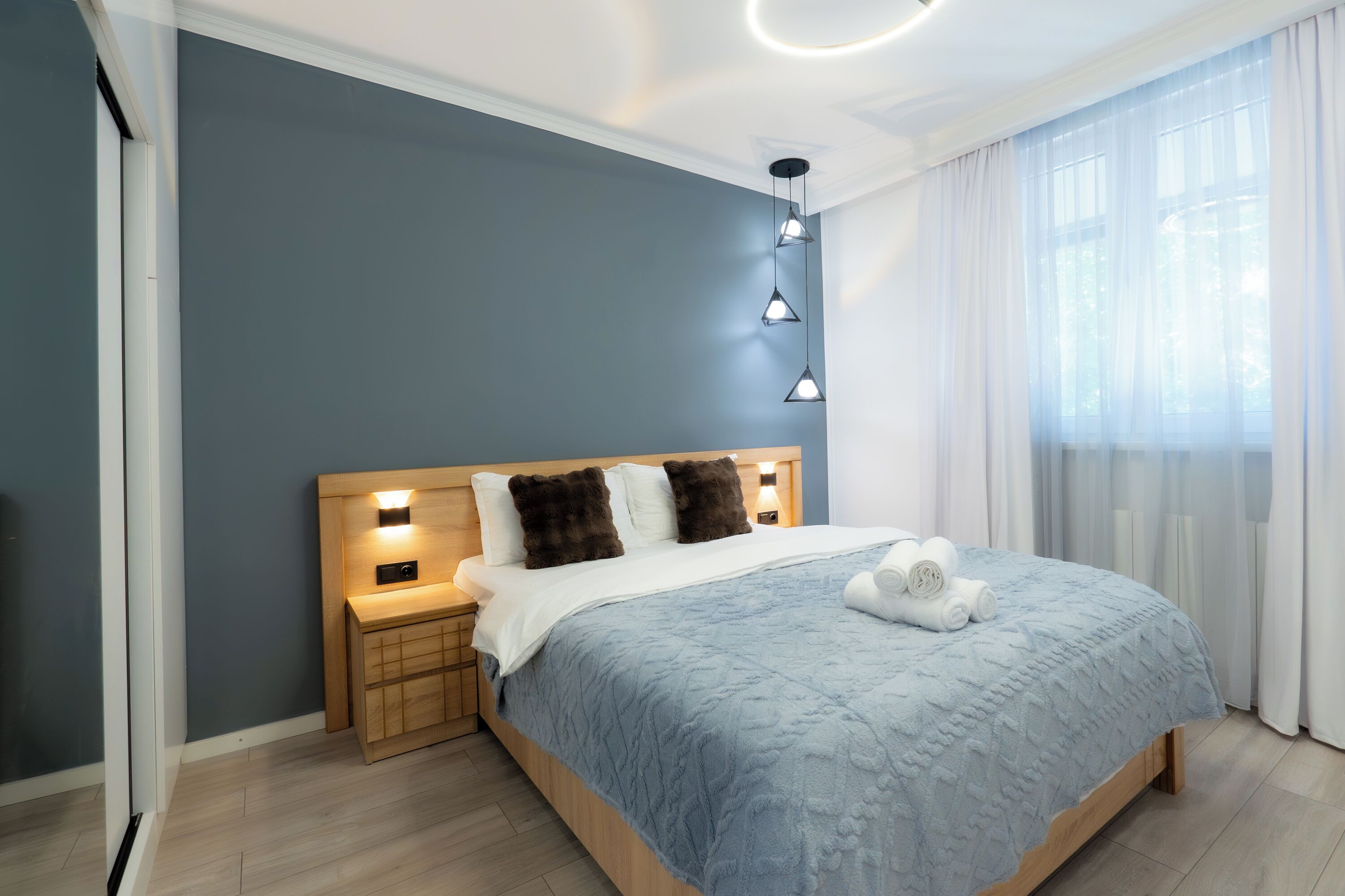 Un letto rifatto con copriletto blu, testiera in legno e due lampade da comodino.
