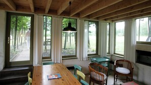 A wooden interior with a large table, chairs, and a fireplace. - Chalet 1 in the heart of an exceptional forest (Jupilles)