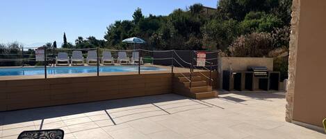 An outdoor swimming pool area with lounge chairs and a barbecue setup.