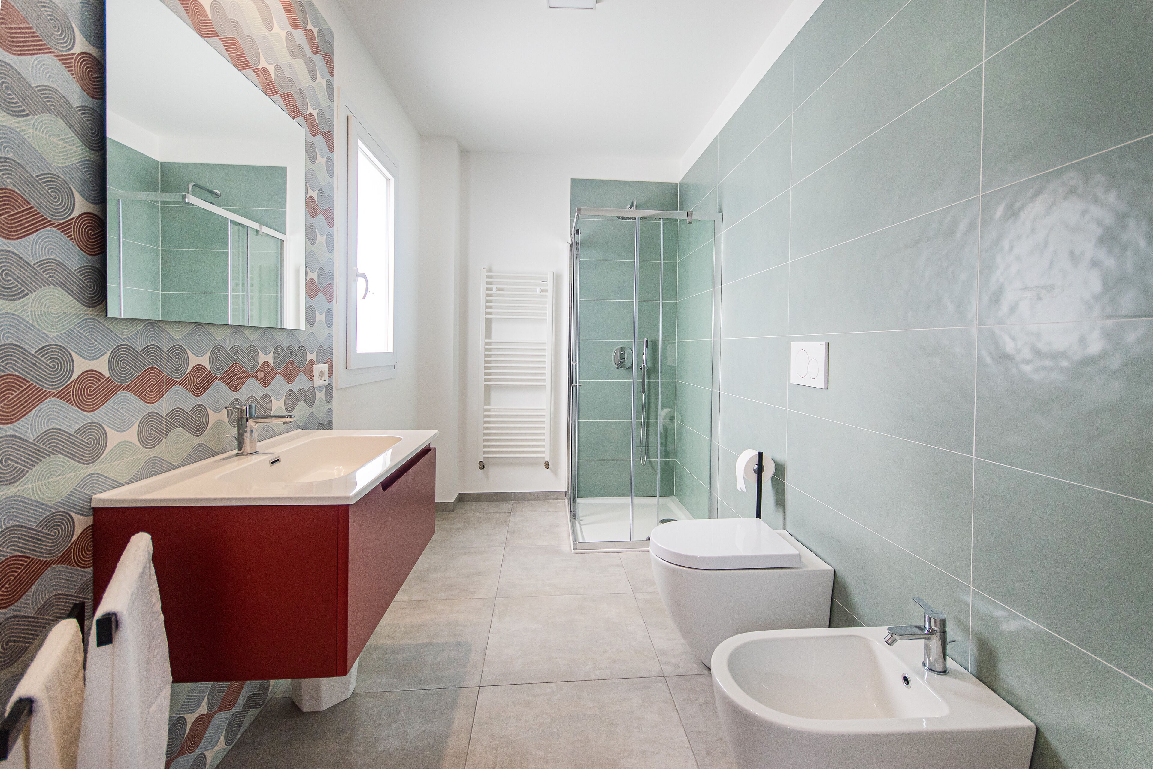 A modern bathroom with a large mirror, a red vanity, a shower, and a bidet.