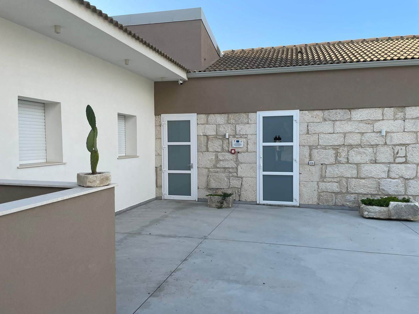 Un edifici amb façana de pedra, dues portes de vidre, una finestra petita i una planta en test.