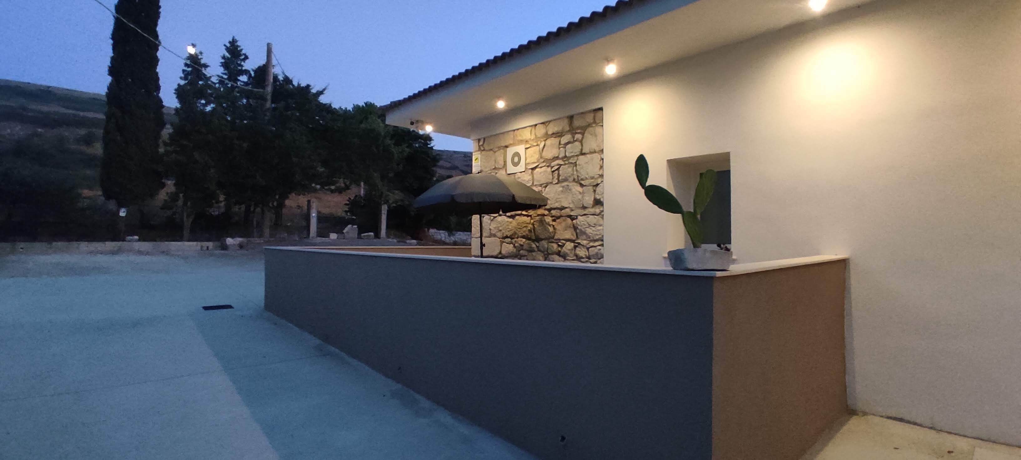 Un espacio exterior moderno con un muro de piedra, una planta de cactus y un pérgola.