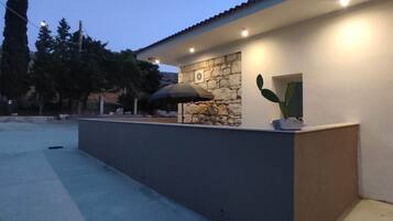 Un espacio exterior moderno con un muro de piedra, una planta de cactus y un pérgola.