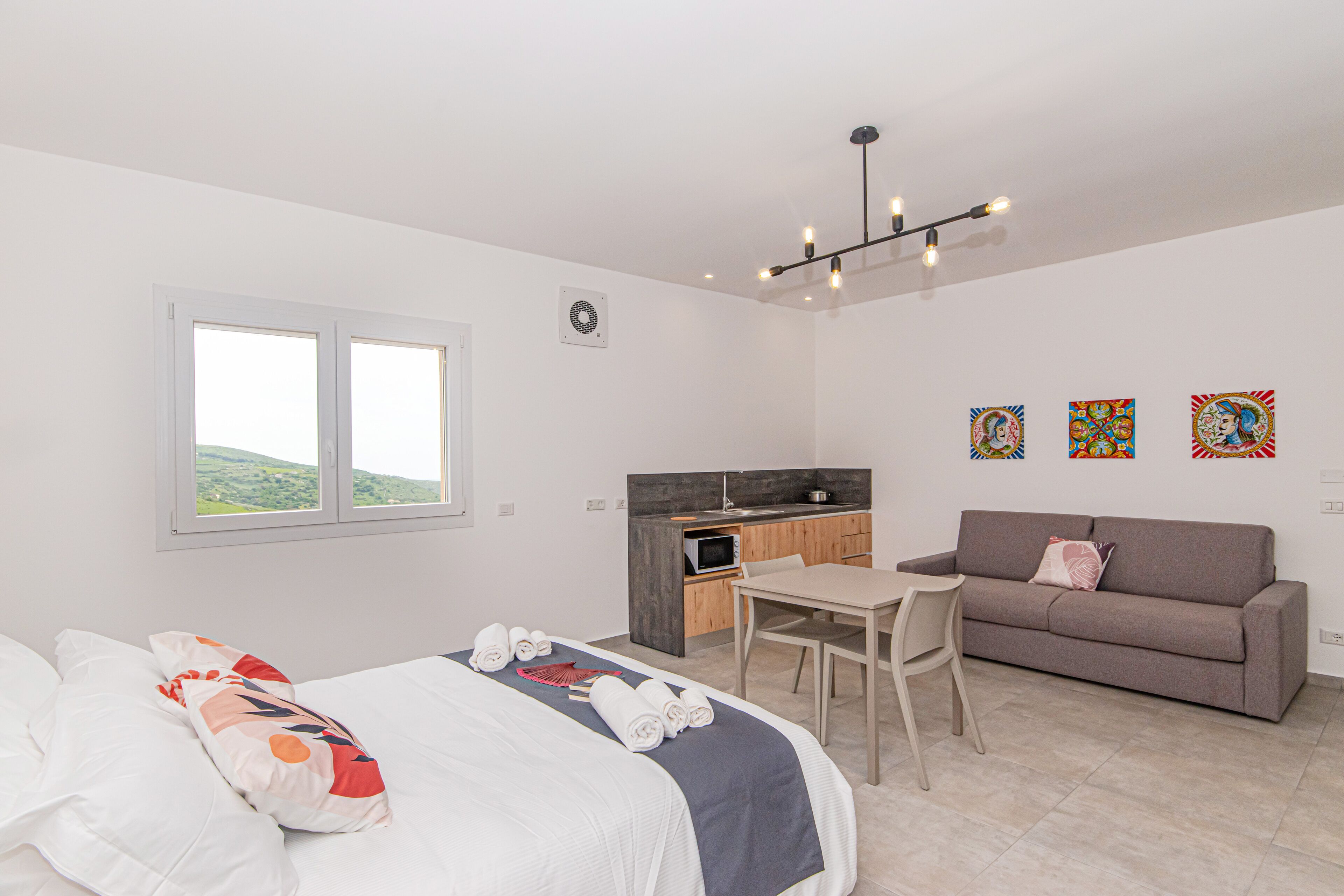 A modern bedroom with a bed, a desk, a sofa, and a kitchenette.