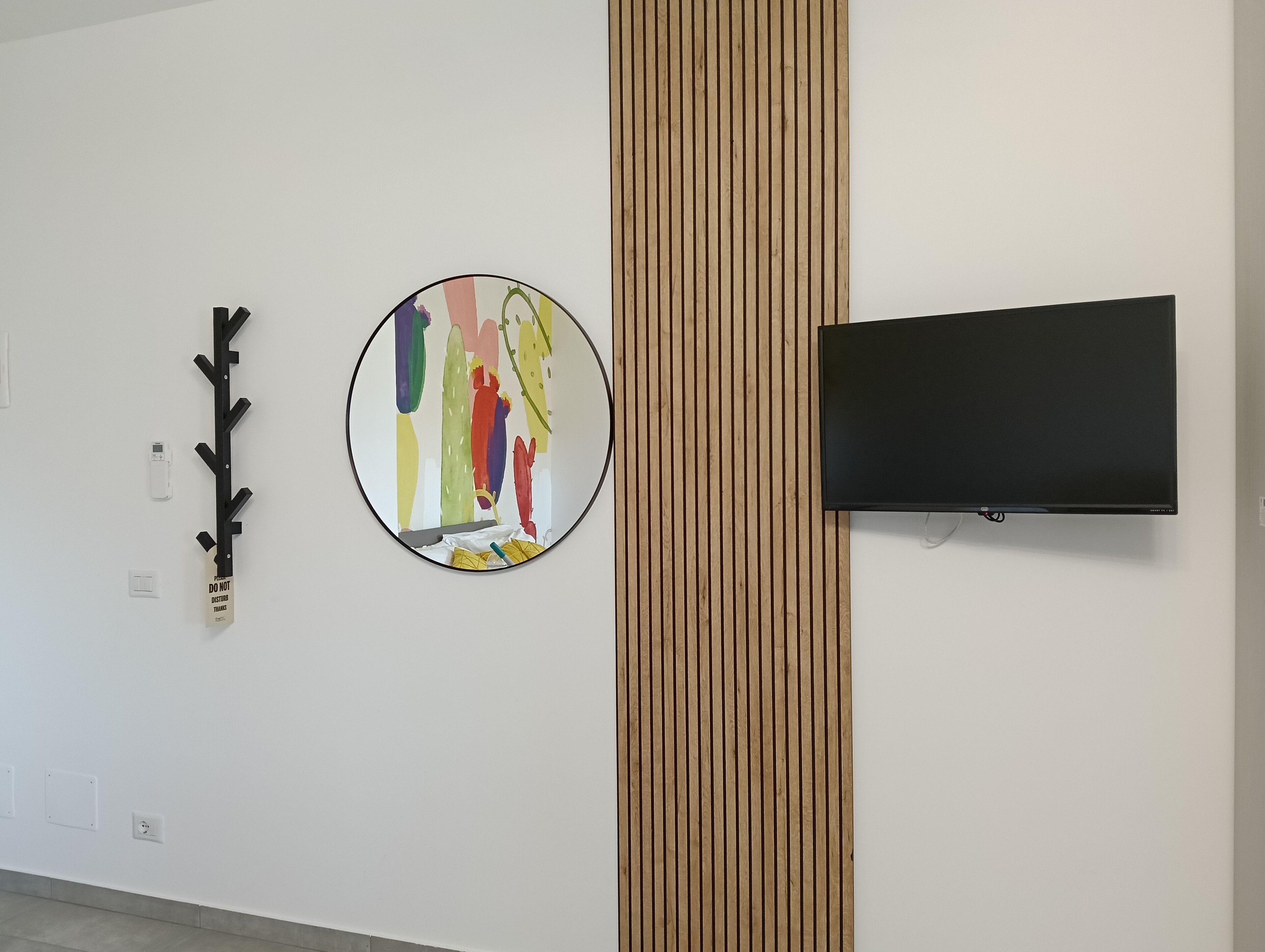 A wall with a round mirror, a black TV, and a wooden panel.