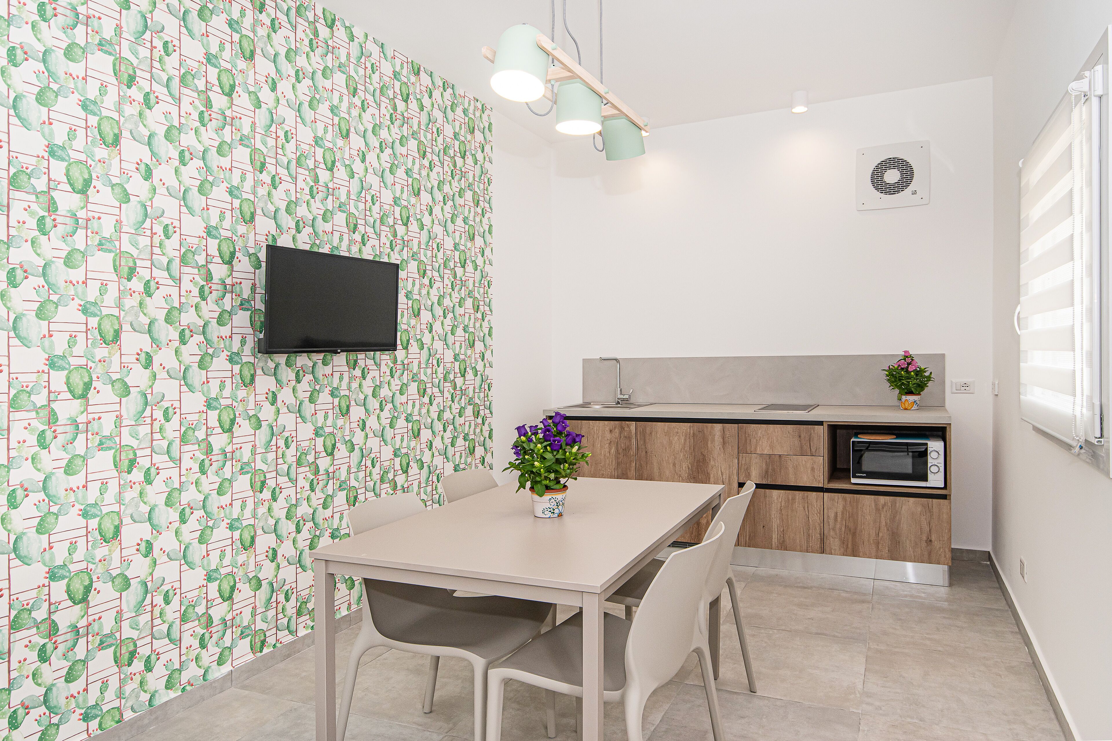 A modern kitchen with a flat-screen TV, wooden cabinets, a microwave, and a dining area with a table and chairs.