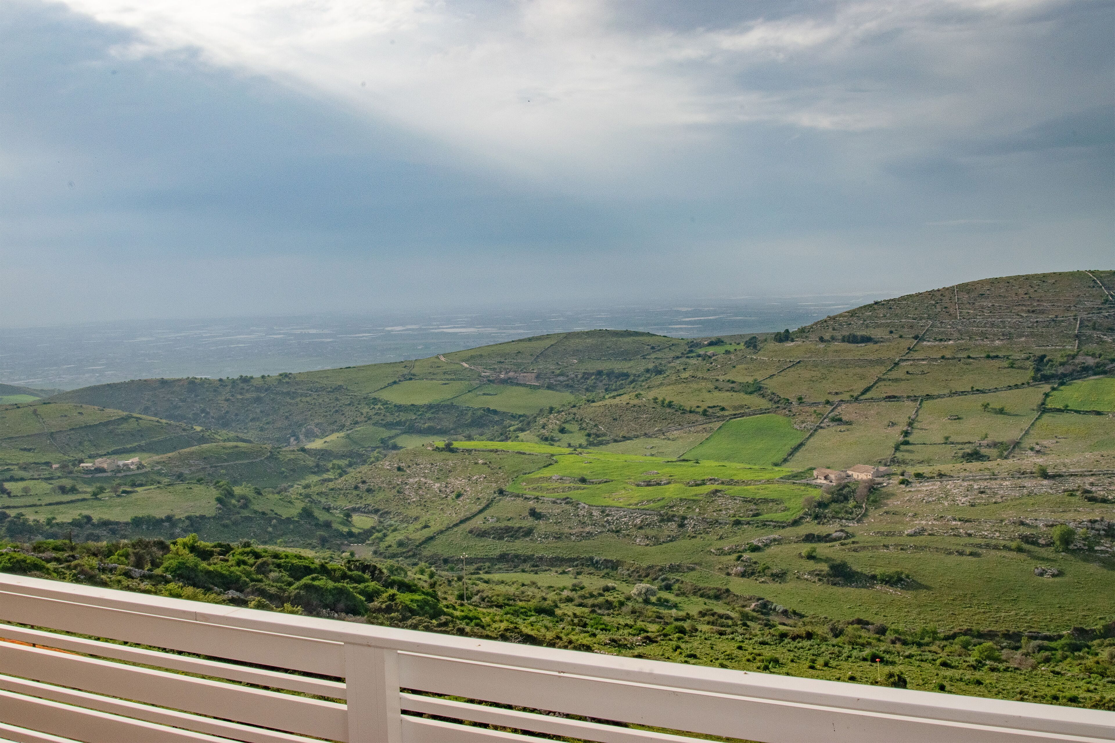 A panoramic view of a hilly landscape with terraced fields and a distant view of the sea.