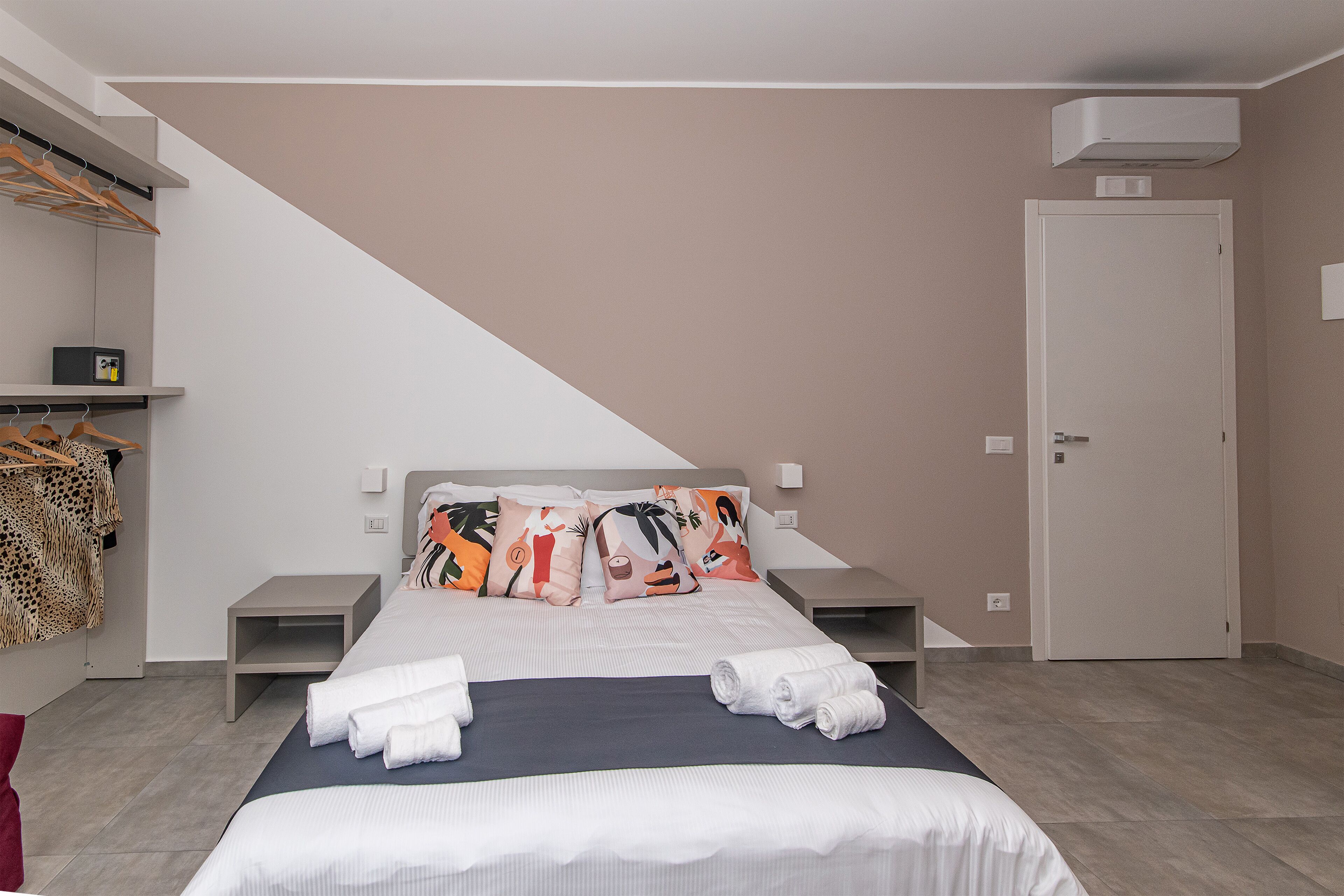 A hotel room with a bed, a wardrobe, a bedside table, and a door.