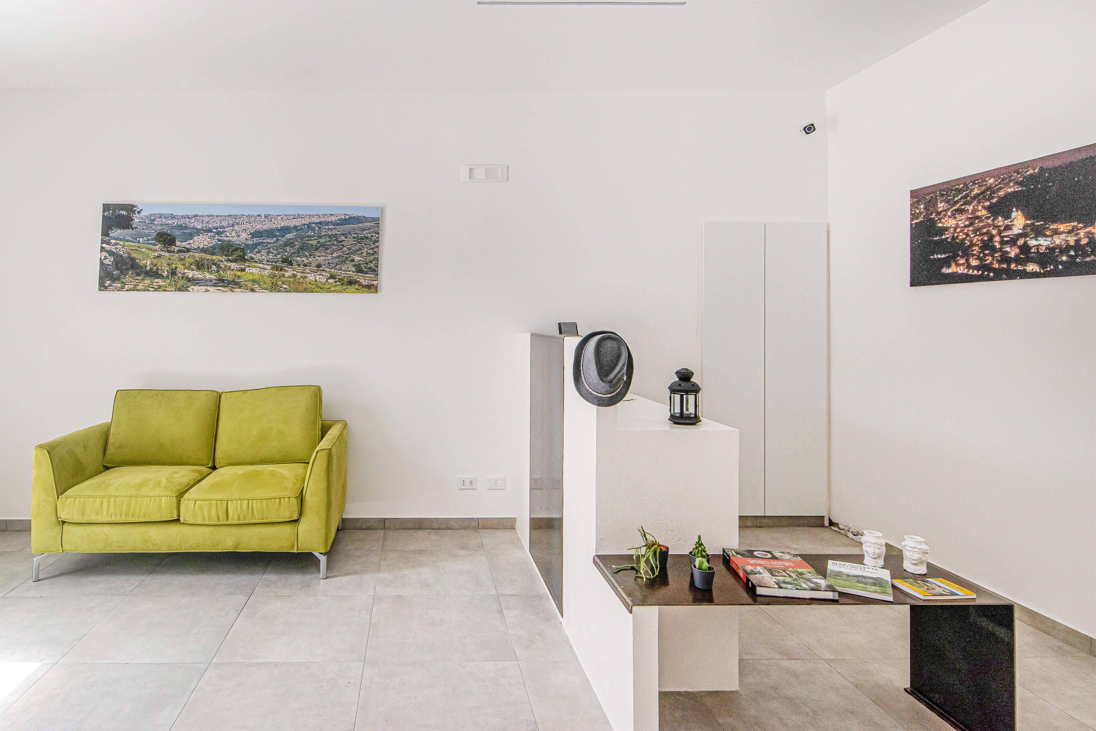 A modern living room with a green sofa, a coffee table with books and decorative items, and two framed pictures on the walls.
