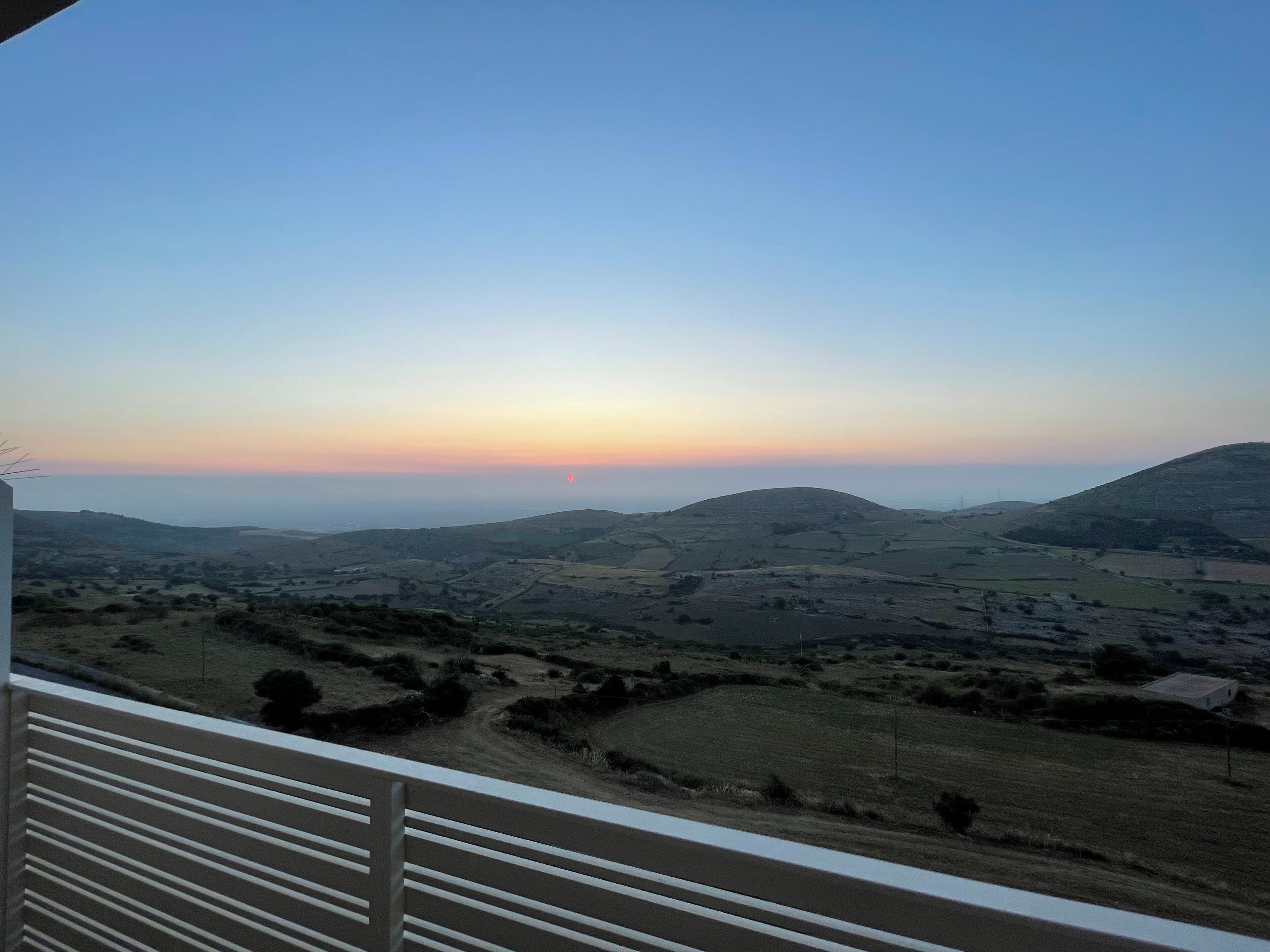 A panoramic view of a hilly landscape with a sunset in the background.