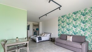 Moderni huone, jossa on sänky, sohva, ruokapöytä tuoleineen ja kuviollinen seinä.
