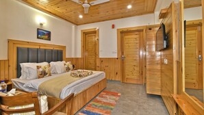 A wooden-paneled room with a bed, a ceiling fan, and a television mounted on the wall. - Hotel Sky Bhagsu (Dharamshala)