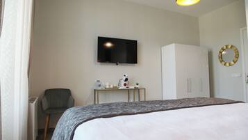 A hotel room with a bed, a desk with a flat-screen TV, a chair, a wardrobe, and a mirror on the wall.