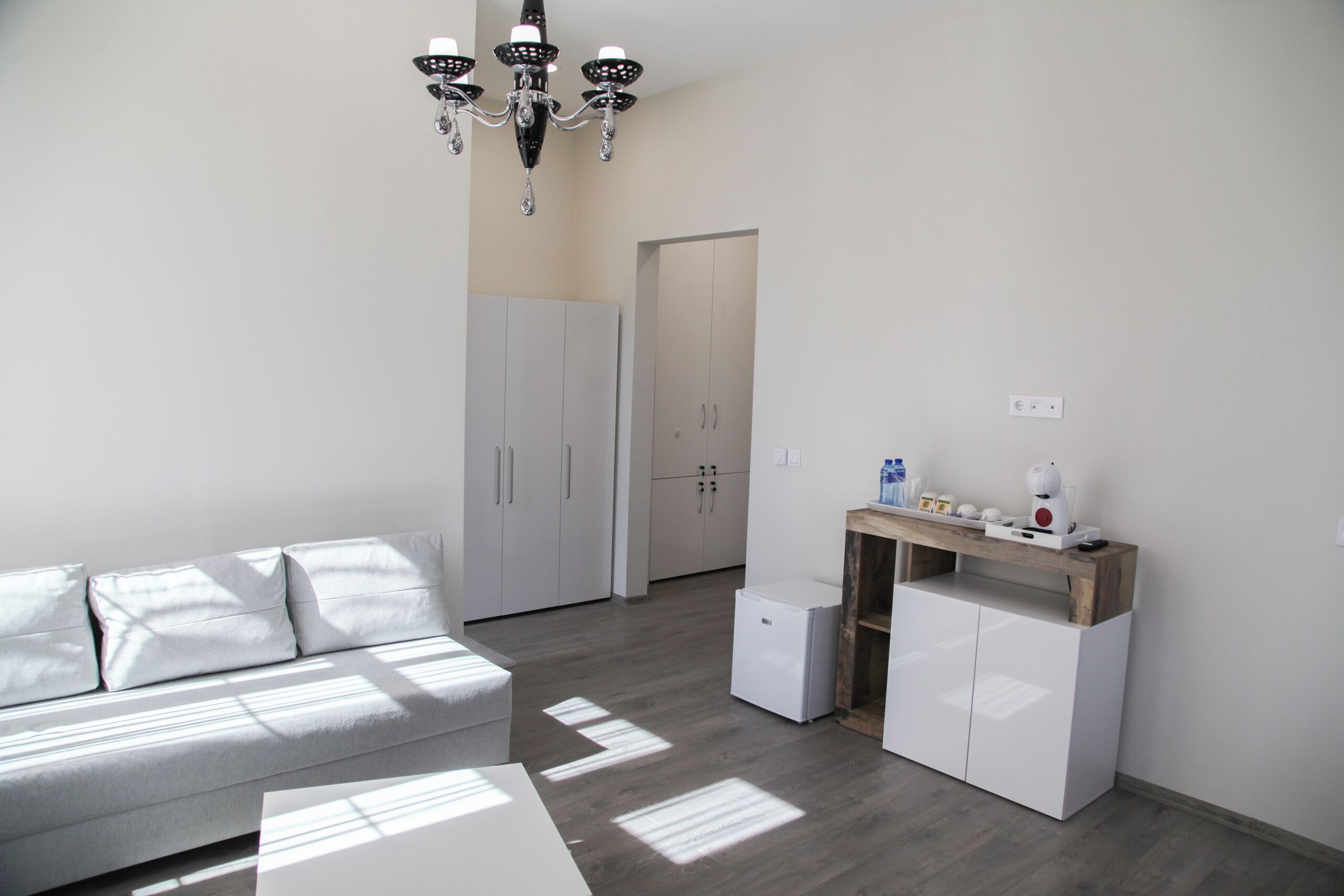 A modern, minimalistic living space with a grey sofa, a small white table, and a built-in wardrobe.