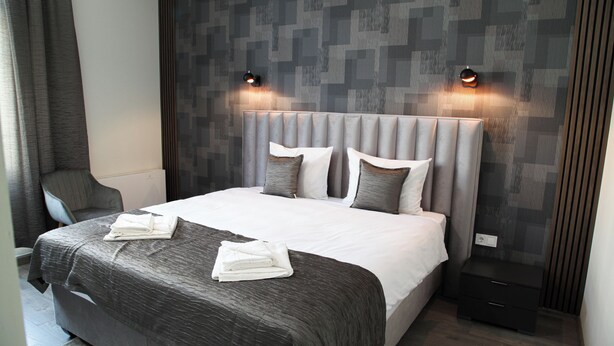 A modern hotel room with a large bed, grey bedding, and two wall-mounted reading lights. - Corner House (Lovech)