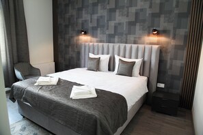 Une chambre d’hôtel moderne avec un grand lit, une literie grise et deux lampes de lecture fixées au mur.