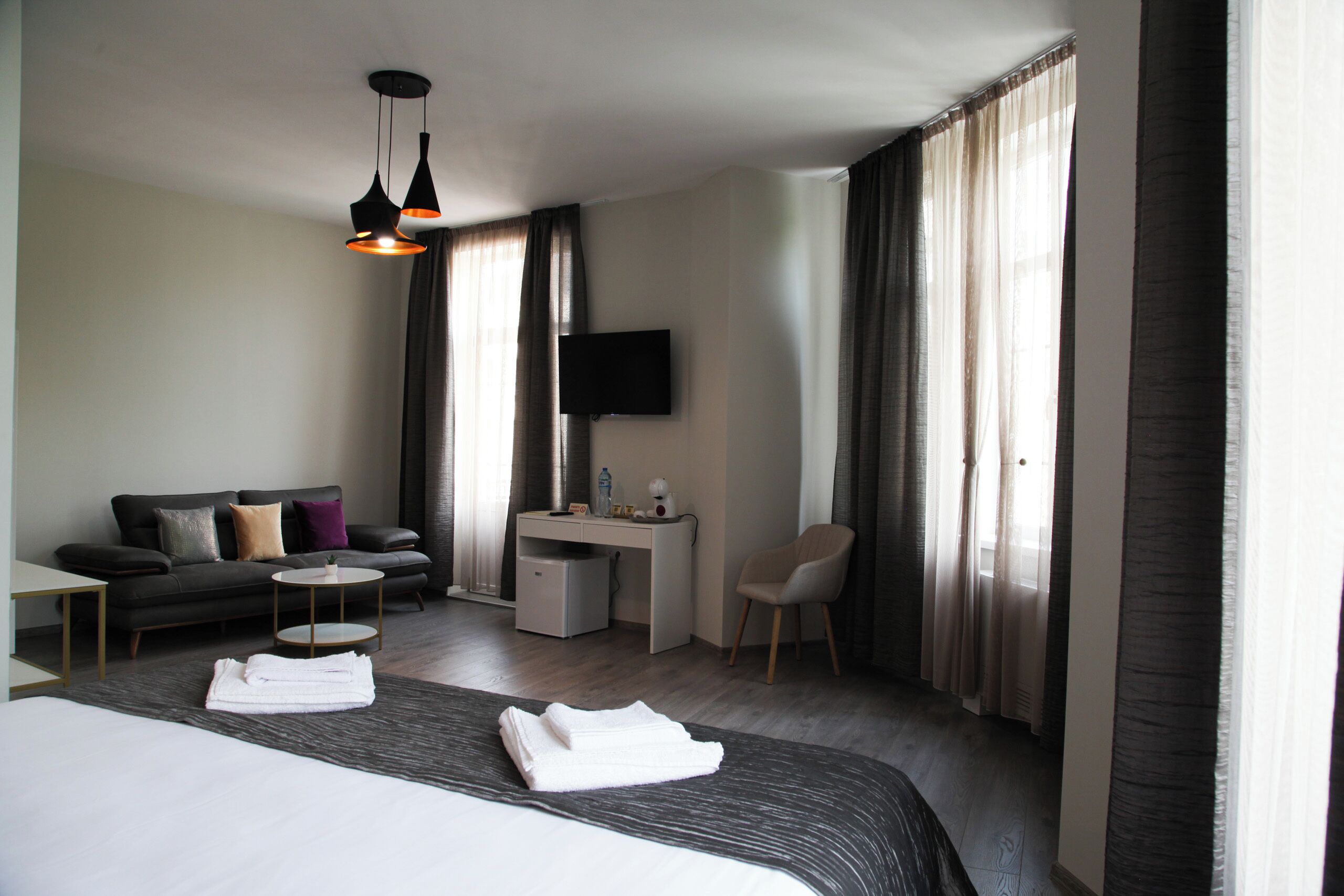 A hotel room with a bed, a sofa, a desk, a chair, a TV, and a window with curtains.