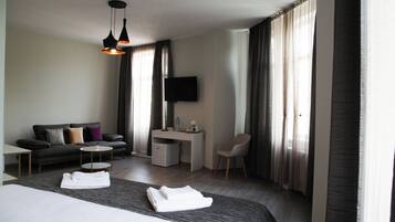 A hotel room with a bed, a sofa, a desk, a chair, a TV, and a window with curtains.
