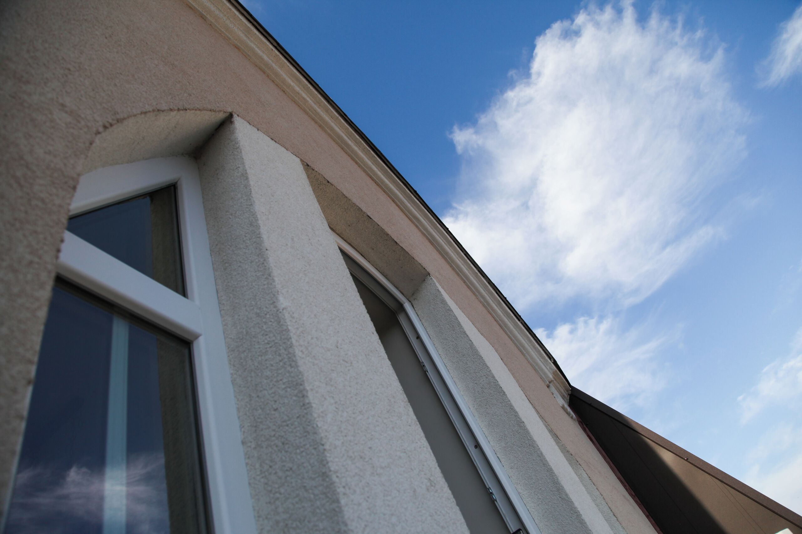 Un angolo di un edificio con una finestra e un cielo sereno con nuvole.