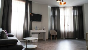 A modern living room with a sofa, a small round table, a desk with a computer, a TV mounted on the wall, and a chair. - Corner House (Lovech)