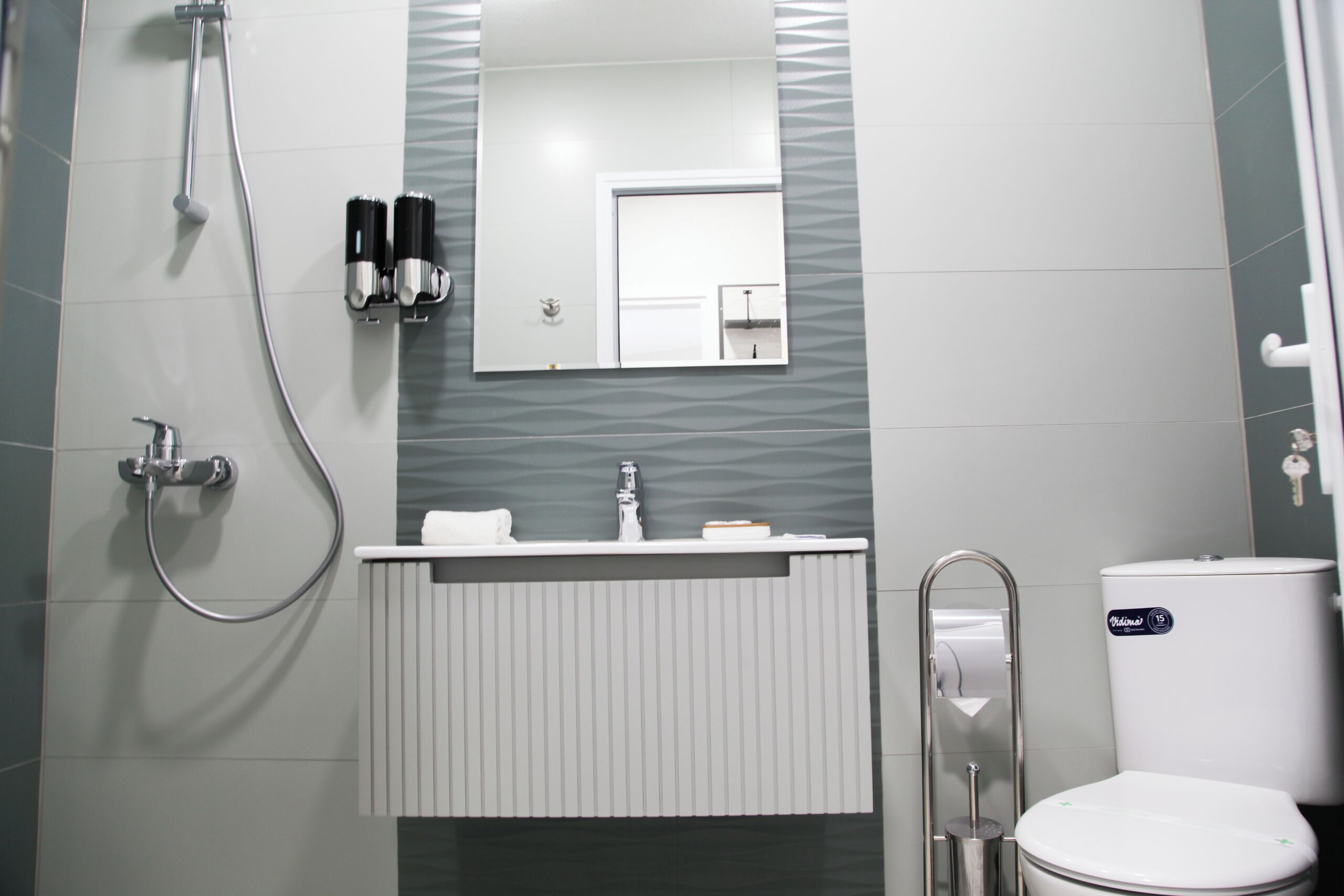 A bathroom with a toilet, a sink with a mirror above it, and a shower area.
