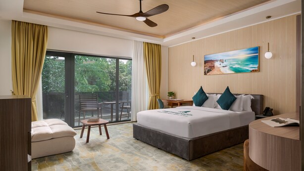 Habitación de hotel con cama, escritorio, silla, mesita y balcón con vistas a zonas verdes.