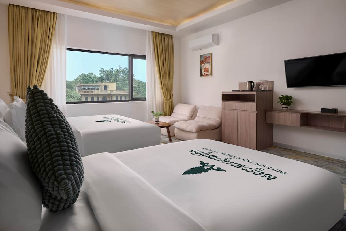 Une chambre d’hôtel avec deux lits, une télévision, un bureau et une vue sur un bâtiment à l’extérieur.