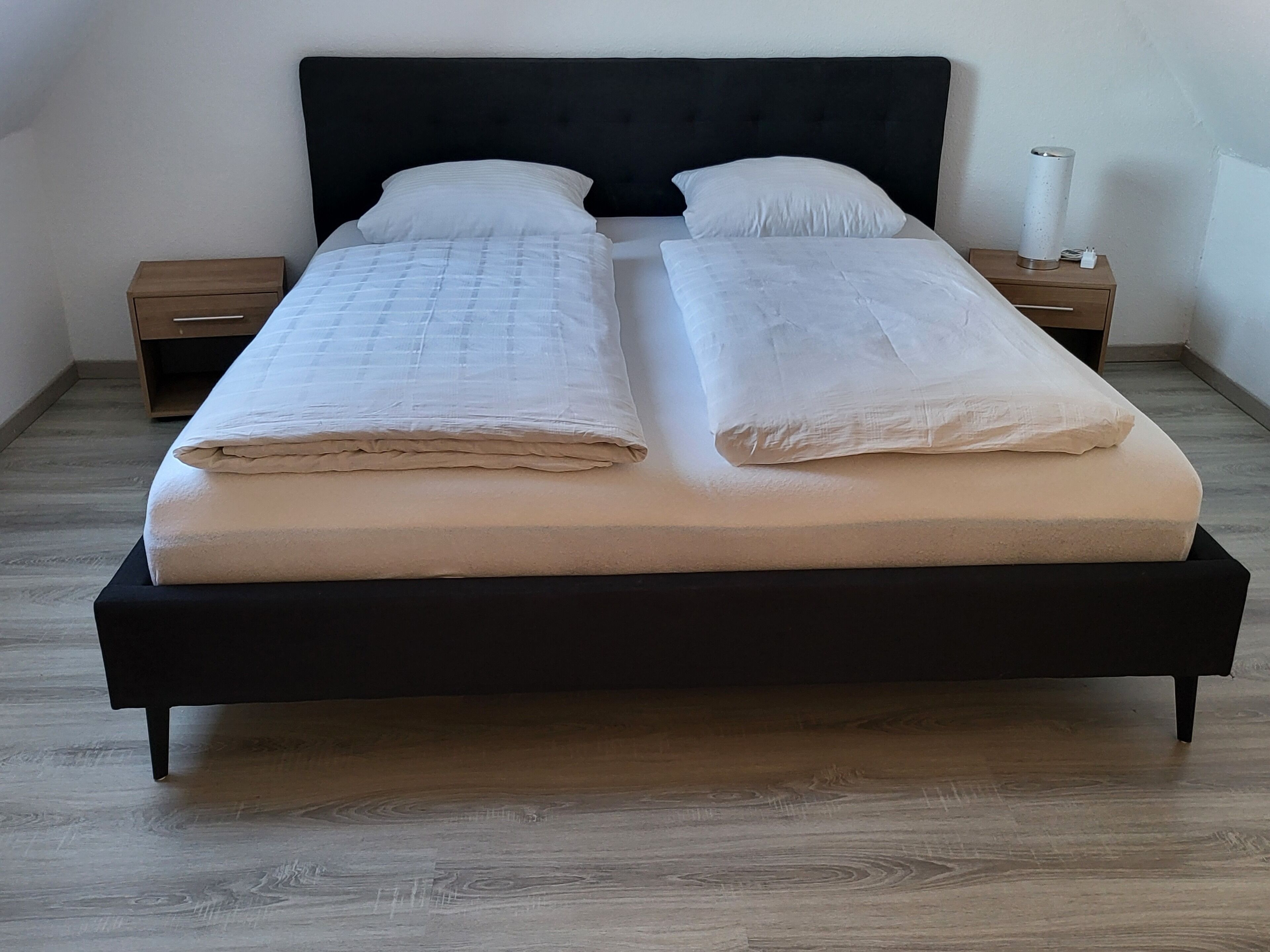 A bed with two pillows, a bedside table, and a lamp.