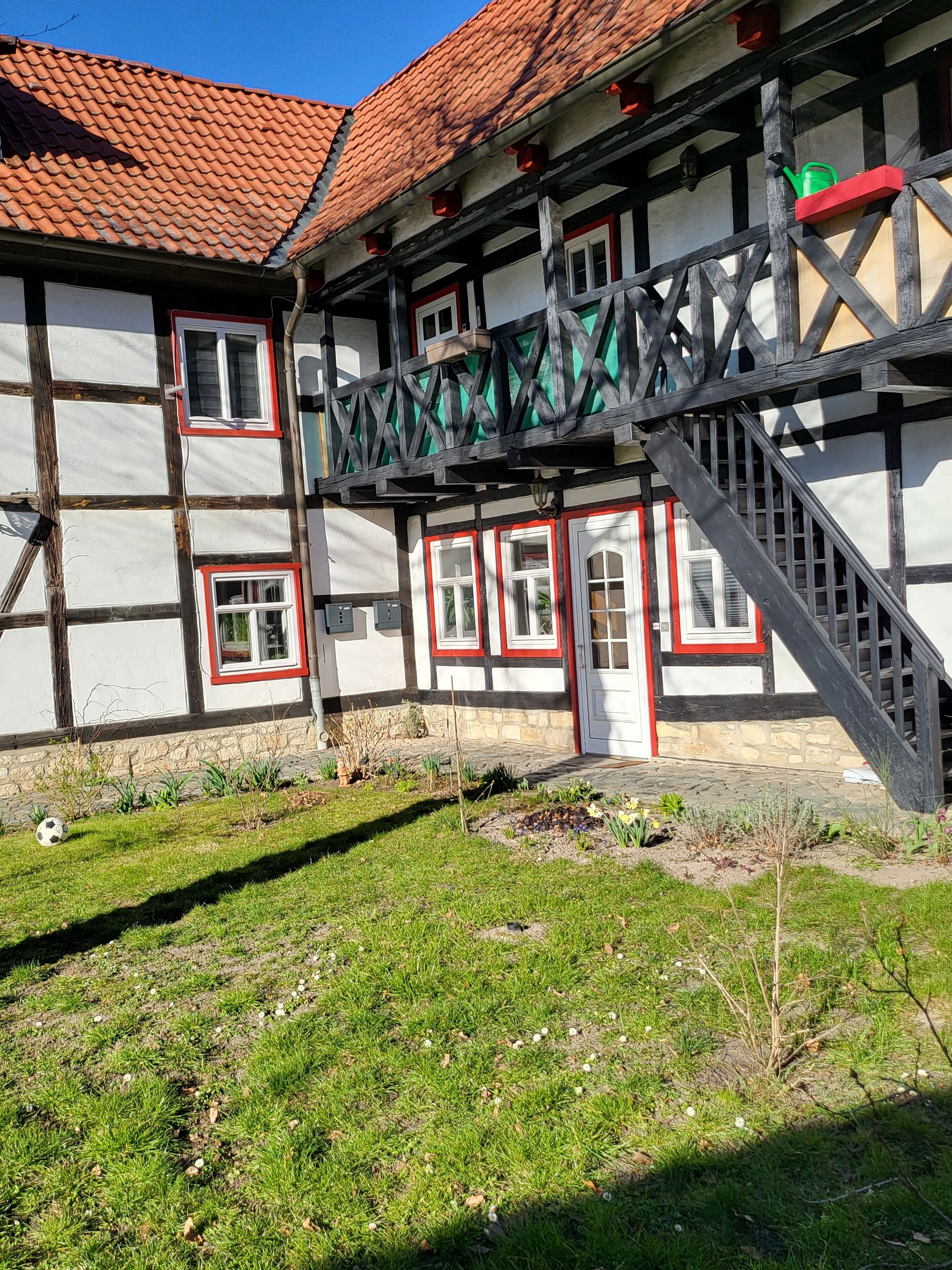 Ein traditionelles Fachwerkhäuschen mit rotem Ziegeldach, einem hölzernen Balkon und einem steinbelagten Weg zum Eingang.