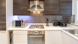 Eine moderne Küche mit dunklen Holzausziehtüren, einer Edelstahl-Dunstabzugshaube, einem Backofen, einem Toaster und einem Wasserkocher.