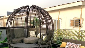 Un área de estar en la azotea con un sillón colgante circular y un sofá con cojines.