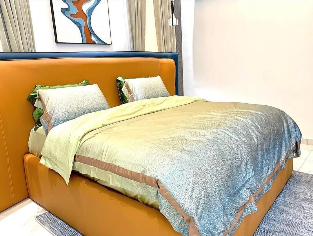 Un lit avec une tête de lit orange, une couverture verte et jaune, et deux oreillers.