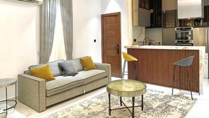 Una sala de estar moderna con un sofá, una mesa de centro redonda y una zona de cocina con barra.