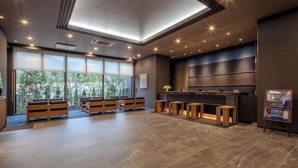 Een moderne hotellobby met een receptiebalie, zithoek en grote ramen met uitzicht op groen.