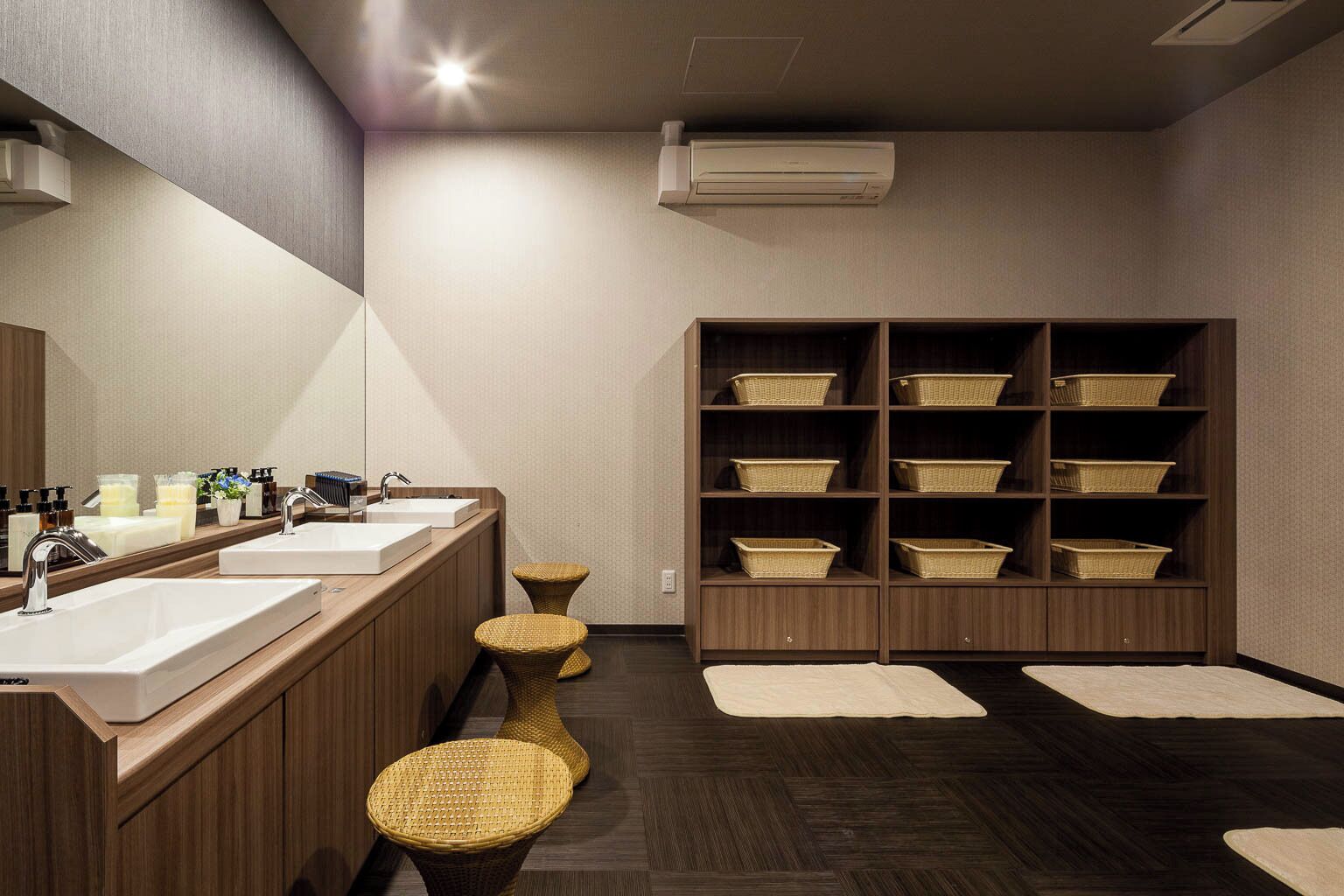 Un baño moderno con dos lavamanos, taburetes de mimbre y un mueble de almacenamiento con cestas.