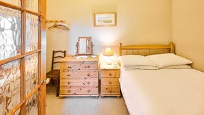 A bedroom with a wooden dresser, a bedside table with a lamp, a bed with white linens, and a framed picture on the wall. - Host Stay The Clock Tower (King's Lynn)