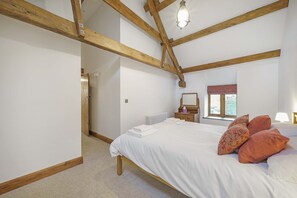 A bedroom with a wooden ceiling, a bed with white bedding, a window with a red valance, and a bedside table with a mirror. - Host Stay The Cart House (Crickhowell)