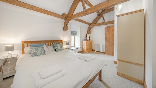 A bedroom with a large bed, wooden beams, a dresser, a radiator, and a wardrobe. - Host Stay The Cart House (Crickhowell)
