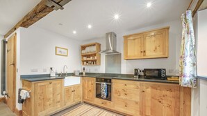 A kitchen with wooden cabinets, a built-in oven, a microwave, and a stainless steel range hood. - Host Stay The Cart House (Crickhowell)