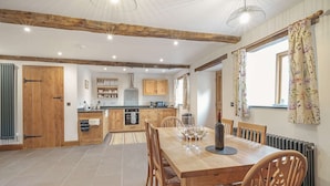 A spacious kitchen with wooden cabinets, a central island, and a dining area with a wooden table and chairs. - Host Stay The Cart House (Crickhowell)