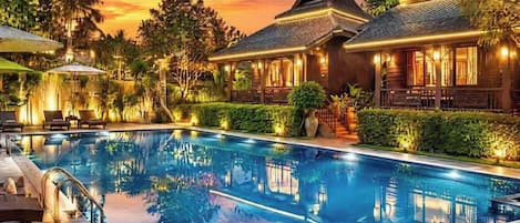 Una piscina con un edificio tradicional al fondo, rodeada de exuberante vegetación.