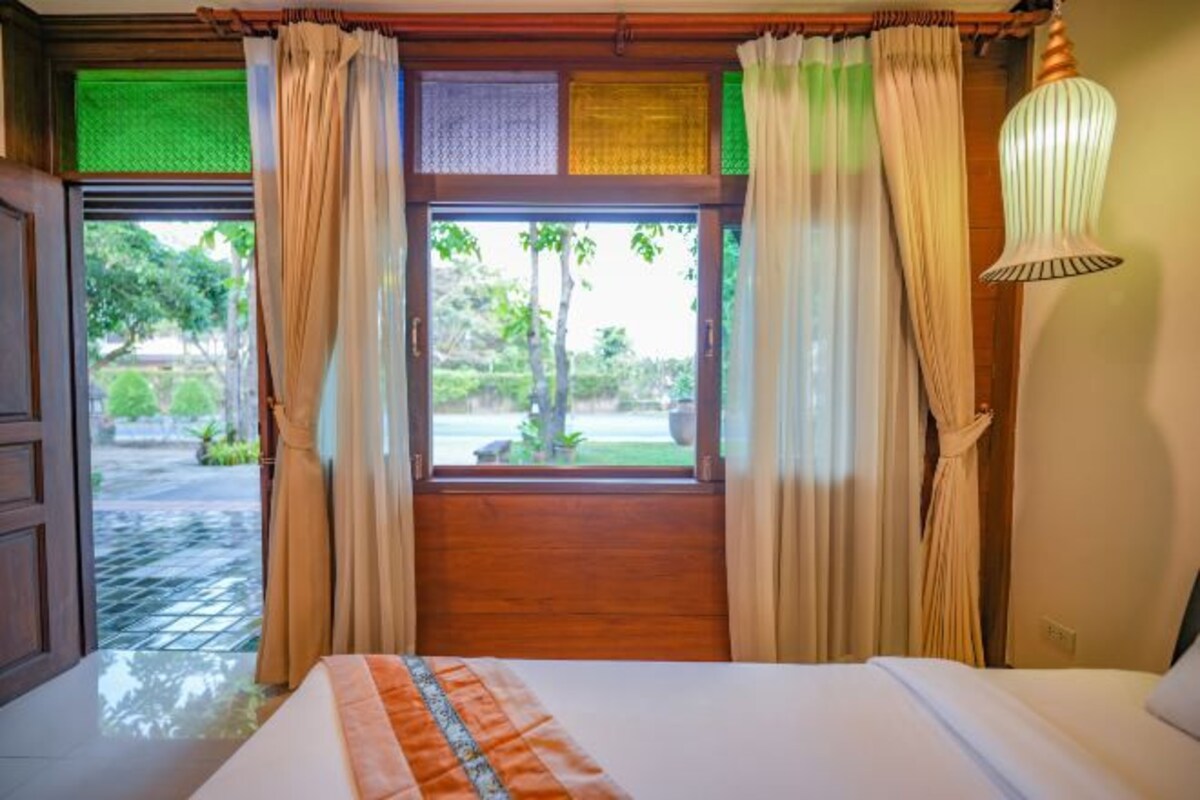 Een hotelkamer met een bed, gordijnen, een raam met uitzicht op groen en een hanglamp.